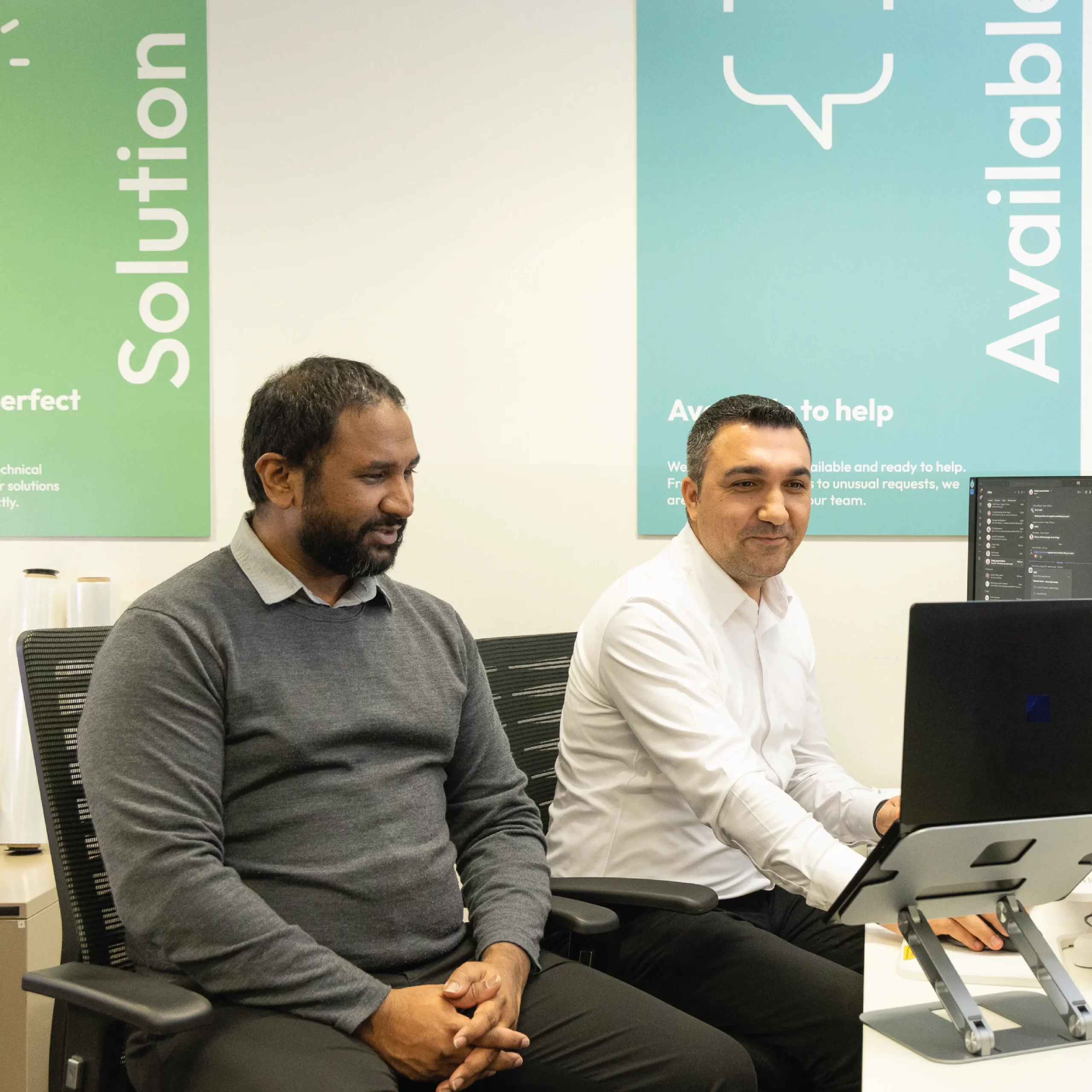 IT experts sitting at a desk looking at a laptop.