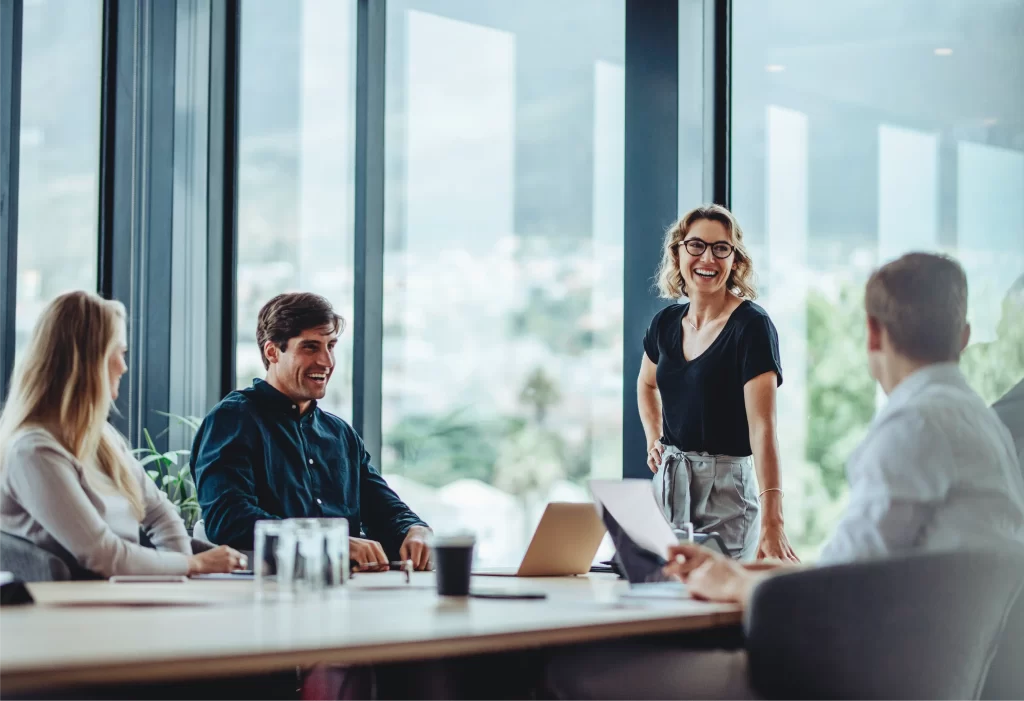 a boardroom with 3 people sitting and one woman standing