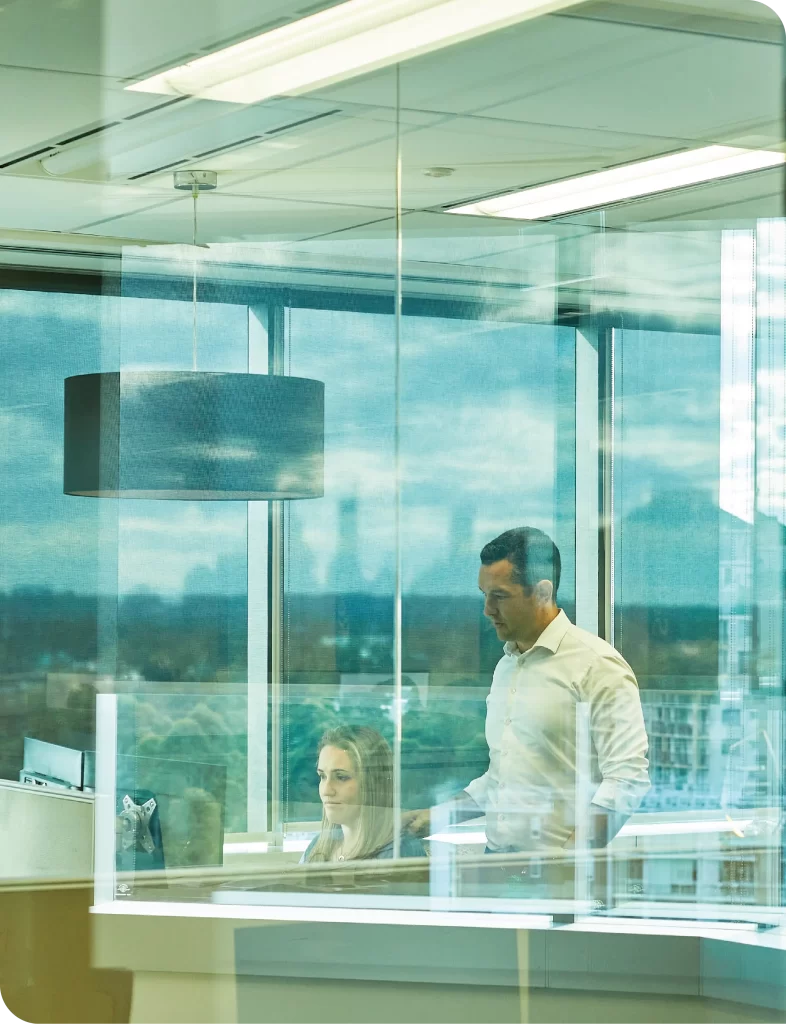 photo through glass of a man standing behind a woman sitting at her desk.